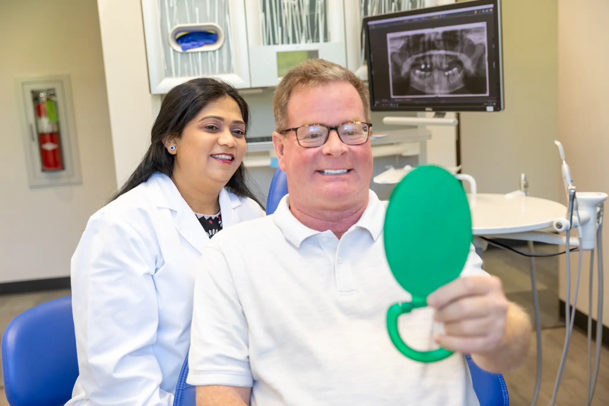 Dr. Vaibhavi Patel with a smiling patient holding a mirror at VSP Dental