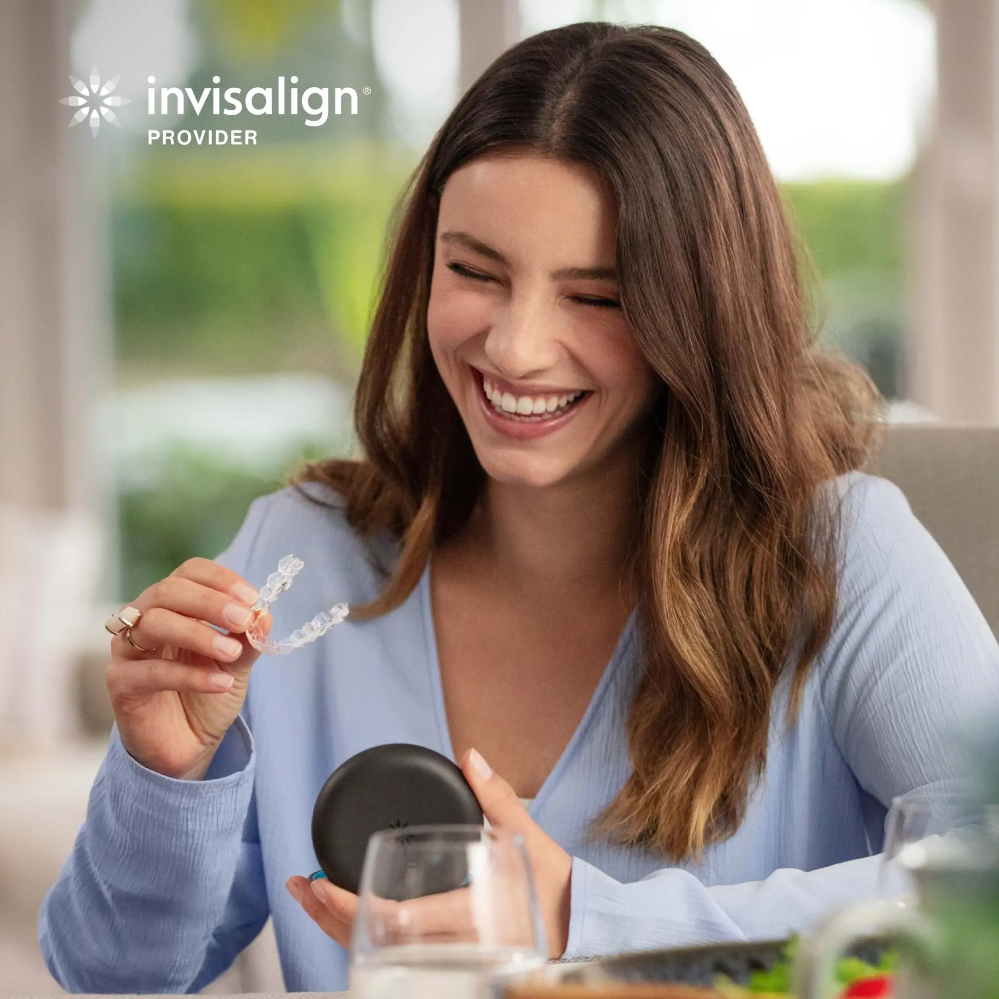 Smiling Invisalign patient holding a clear aligner